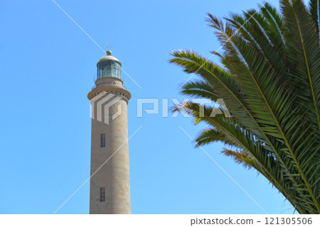 A lighthouse Faro against blue sky with a palm tree at the foreground in Maspalomas, Gran Canaria, Canary Islands, Spain A lighthouse Faro against blue sky with a palm tree at the foreground in Maspalomas, Gran Canaria, Canary Islands, Spain 121305506