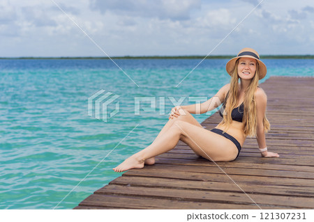 Woman in swimsuit sitting on a pier at Lake Bacalar. Quintana Roo, Mexico travel, summer relaxation, and waterfront serenity concept 121307231