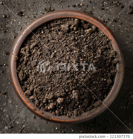 Rich, dark soil fills a terracotta pot, showing texture and potential for gardening at a vibrant outdoor location 121307370