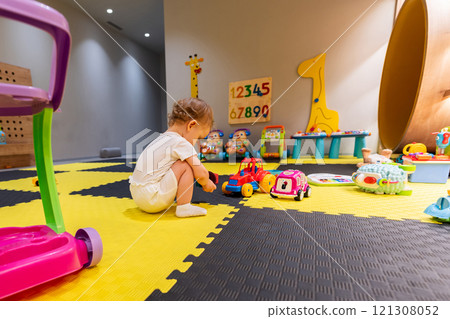 oddler sitting on a playmat surrounded by toys in a vibrant playroom. Concept of early childhood development and fun activities oddler sitting on a playmat surrounded by toys in a vibrant playroom. Concept of early childhood development and fun activities 121308052