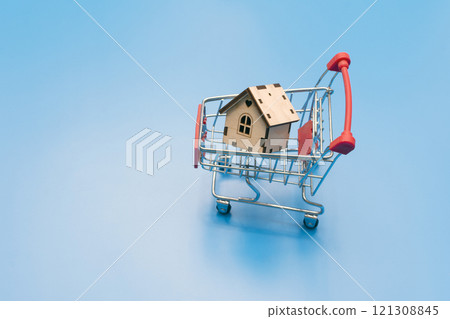 small wooden decorative house in a shopping cart on a blue background. purchase concept small wooden decorative house in a shopping cart on a blue background. purchase concept 121308845