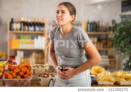 Young woman with stomach pain in grocery store Young woman with stomach pain in grocery store 121309170