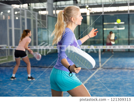 Sporty woman padel player hitting ball with a racket on hard court Sporty woman padel player hitting ball with a racket on hard court 121309313