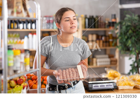 Young woman choosing raw sausages in grocery store Young woman choosing raw sausages in grocery store 121309330