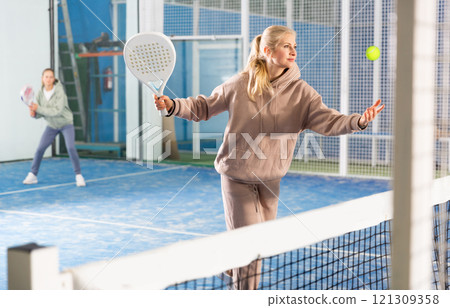 Woman serving ball while playing padel in court 121309358