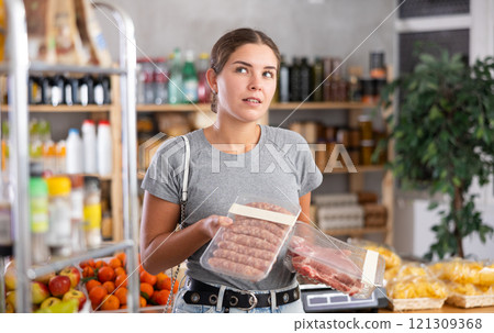 Female shopper chooses between raw sausages and pork in grocery supermarket Female shopper chooses between raw sausages and pork in grocery supermarket 121309368