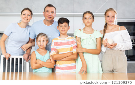 Happy dad and mum with three daughters and son is standing near kitchen table. Happy dad and mum with three daughters and son is standing near kitchen table. 121309370