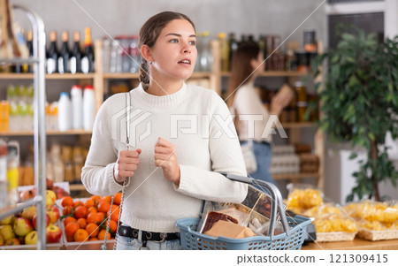 Portrait of girl shopper with a shopping cart choosing some products in supermarket Portrait of girl shopper with a shopping cart choosing some products in supermarket 121309415