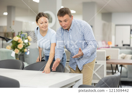 Enthusiastic man and woman choosing dining table in furniture store 121309442