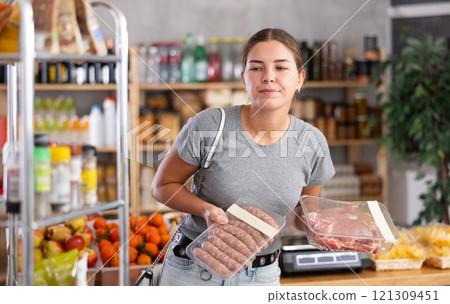 Young woman choosing raw sausages and pork in grocery store 121309451