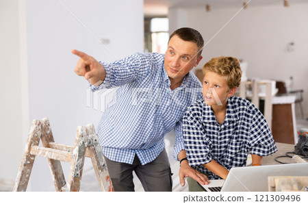 Man architect and boy using laptop while discussing working process in house being renovated Man architect and boy using laptop while discussing working process in house being renovated 121309496