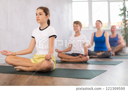 School children and their parents sitting on mats in Lotus pose during family yoga training in gym fitness center indoors 121309500