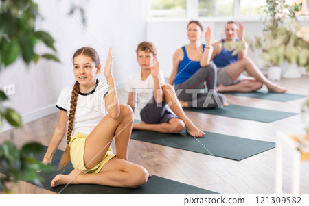 Pleasant preteen girl practicing half lord of the fishes pose of yoga with her family 121309582