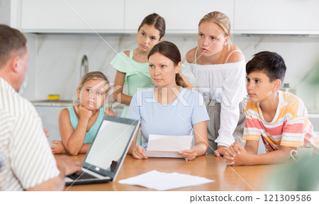 Man with laptop does remote work, frustrated wife reads letter, and alarmed children stand nearby Man with laptop does remote work, frustrated wife reads letter, and alarmed children stand nearby 121309586