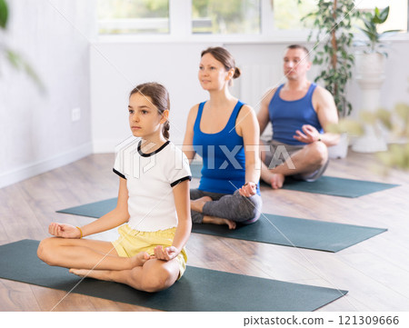 Teenage girl with her parents practices yoga in lotus position 121309666