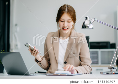 Asian businesswoman working with working notepad, tablet and laptop documents talking on the smartphone, tablet and laptop video call tax 121310897