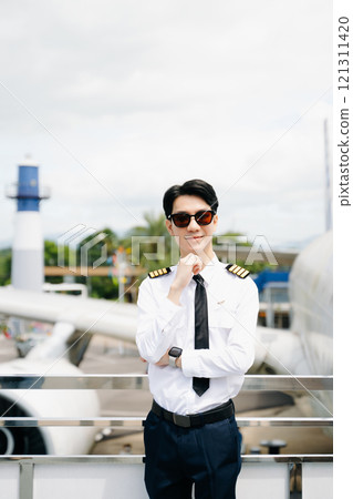 Asian Confident male pilot in uniform leaning at the passenger seat while standing inside of the airplane flight cockpit during takeoff and checking 121311420