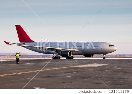 Airport marshaller meets passenger jet plane that taxiing to the parking place in a cold winter weather Airport marshaller meets passenger jet plane that taxiing to the parking place in a cold winter weather 121311579