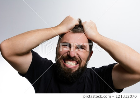 Man experiencing frustration and stress, pulling his hair in anguish against a light background. 121312070