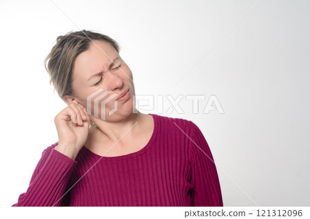Woman experiencing ear discomfort, touching her ear with a pained expression. Woman experiencing ear discomfort, touching her ear with a pained expression. 121312096
