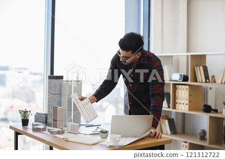 Indian male architect focuses on creating detailed city model for modern urban development, showcasing creativity and precision in office environment with natural light. Indian male architect focuses on creating detailed city model for modern urban development, showcasing creativity and precision in office environment with natural light. 121312722