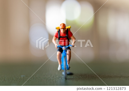 Close-up shot of a figurine of a cyclist riding a blue bicycle with a backpack Close-up shot of a figurine of a cyclist riding a blue bicycle with a backpack 121312873