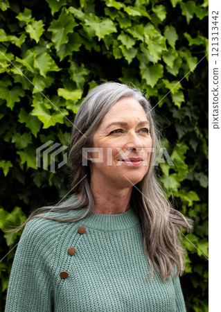 Smiling mature woman enjoying nature, standing outdoors with green leaves background Smiling mature woman enjoying nature, standing outdoors with green leaves background 121313442