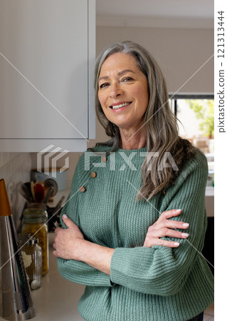 Smiling mature woman in cozy sweater standing confidently in kitchen, at home Smiling mature woman in cozy sweater standing confidently in kitchen, at home 121313444