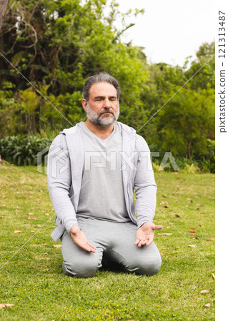 Mature man meditating outdoors on grass, finding peace and relaxation 121313487