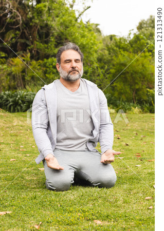 Mature man meditating outdoors on grass, finding peace and relaxation 121313490