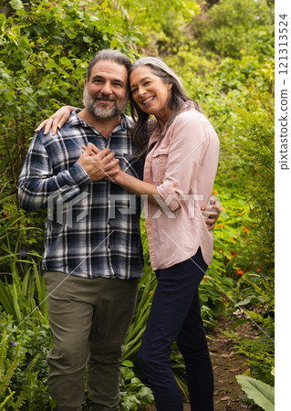 Happy mature couple embracing in lush garden, enjoying nature together, outdoors 121313524