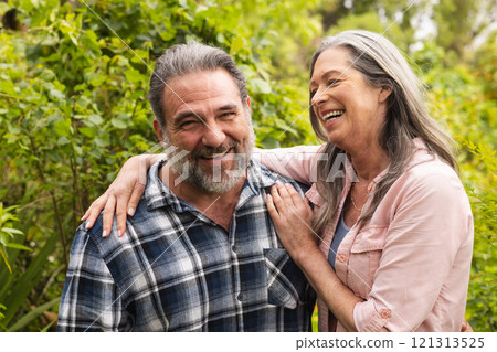 Happy mature couple laughing together in lush garden, enjoying outdoor moments 121313525