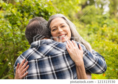 Happy mature couple embracing outdoors, woman smiling joyfully in lush garden Happy mature couple embracing outdoors, woman smiling joyfully in lush garden 121313530