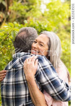 Mature couple embracing outdoors, woman smiling warmly in lush garden Mature couple embracing outdoors, woman smiling warmly in lush garden 121313531