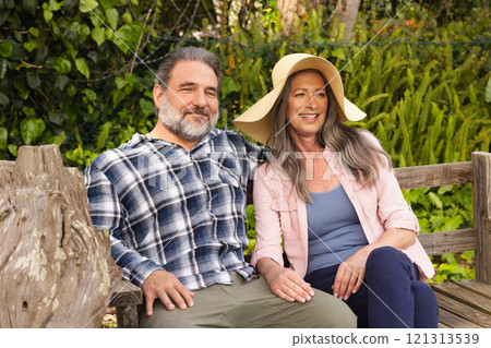 Smiling mature couple sitting on garden bench enjoying sunny day together, outdoors 121313539