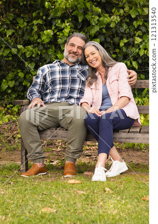 Happy mature couple sitting on park bench, enjoying peaceful moment together, outdoors 121313540