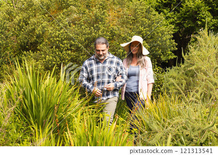 Mature couple walking through lush garden, enjoying peaceful nature together, outdoors 121313541