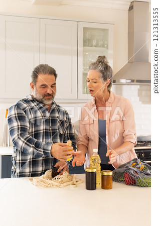 Mature couple organizing groceries in kitchen, sharing conversation and smiles, at home 121313555