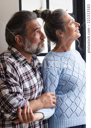 Mature couple gazing out window, enjoying peaceful moment at home together 121313583