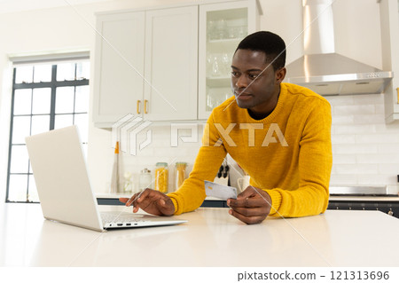 African american man in kitchen shopping online with laptop and credit card, at home African american man in kitchen shopping online with laptop and credit card, at home 121313696