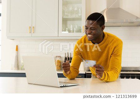 Smiling African american man shopping online with credit card in modern kitchen, at home Smiling African american man shopping online with credit card in modern kitchen, at home 121313699