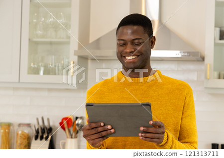 Smiling African american man in kitchen using tablet, enjoying holiday season at home Smiling African american man in kitchen using tablet, enjoying holiday season at home 121313711