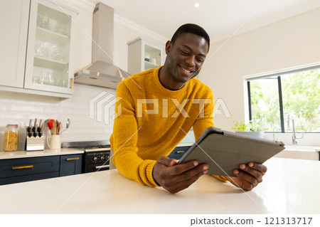 Smiling African american man in kitchen using tablet, enjoying leisure time at home Smiling African american man in kitchen using tablet, enjoying leisure time at home 121313717