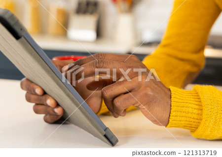 African american man in yellow sweater using tablet at home, focusing on screen African american man in yellow sweater using tablet at home, focusing on screen 121313719