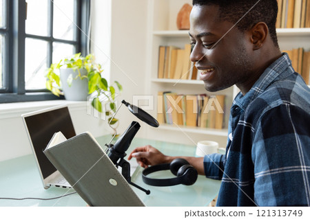 Smiling African american man recording podcast at home with microphone and laptop 121313749
