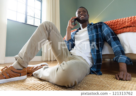 At home, African American man sitting on floor, talking on smartphone, smiling 121313762