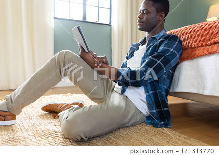 Relaxing at home, young African american man reading tablet by bed, enjoying leisure time Relaxing at home, young African american man reading tablet by bed, enjoying leisure time 121313770