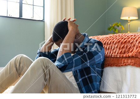 African American man sitting on bedroom floor, looking stressed and overwhelmed, at home 121313772