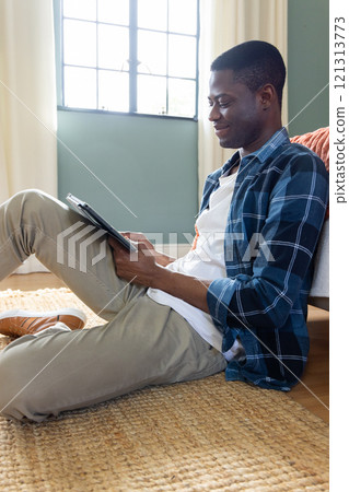 Relaxing at home, African American man using tablet and smiling on rug Relaxing at home, African American man using tablet and smiling on rug 121313773