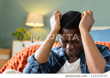 At home, African American man feeling stressed, sitting on couch with hands on head At home, African American man feeling stressed, sitting on couch with hands on head 121313775